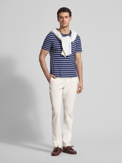 Męski model nosi Slim Fit Chino aus Baumwoll-Mix od Tommy Hilfiger, jasny kolor, krój slim fit, detale: pasek, logo, przód, ujęcie całopostaciowe z przodu.