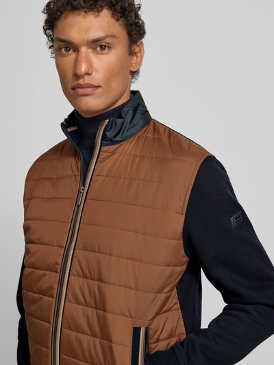 Männermodel draagt Sweatjacke mit Label-Detail van Bugatti in katoenmix, regular fit, ribboorden, opstaande kraag, ritssluiting, ritszakken, kleur bruin en donkerblauw, ruglengte maat M 68 cm, mouwlengte 67 cm, nahaufnahme bovenlichaam.