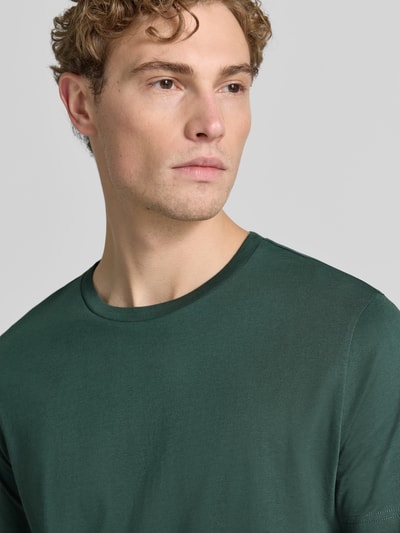 Męski model nosi T-Shirt aus Baumwolle mit Rundhalsausschnitt von Christian Berg Men, krój slim fit, ciemnozielony, okrągły dekolt, miękka bawełna, długość tyłu w rozmiarze M: 73 cm, zbliżenie na górną część ciała z przodu.