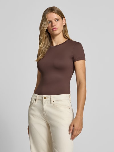 Vrouwenmodel draagt bruin slim fit t-shirt met ronde hals model 'LULA' van PIECES dames, voorkant heupopname.