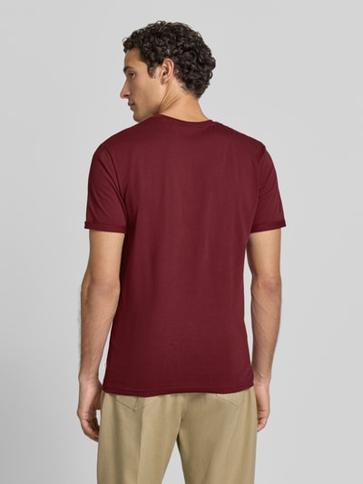 Männermodel trägt T-Shirt mit Logo-Stitching und Rundhalsausschnitt von Les Deux, Bordeaux, Straight Fit, Ganzkörperansicht Rückansicht, Baumwoll-Mix mit Stretch-Anteil, Rückenlänge bei Größe M 70 cm, Label-Detail.