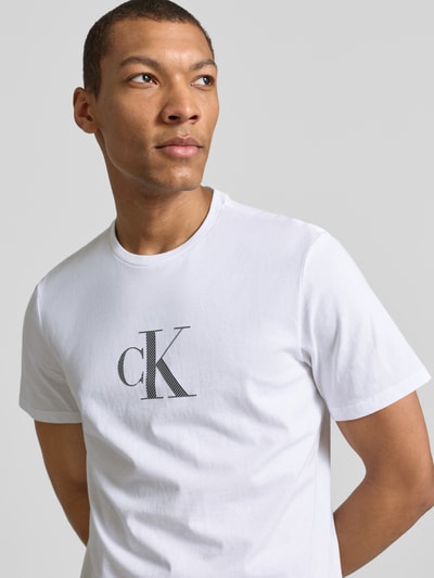 Männermodel trägt weißes T-Shirt mit Rundhalsausschnitt und Logo von CK Calvin Klein, Regular-Fit, reine Baumwolle, Nahaufnahme Oberkörper.
