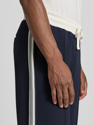 Männermodel trägt Straight Fit Sweatpants mit Elastikbund von MCNEAL in Dunkelblau mit weißen Streifen, seitliche Eingrifftaschen, Nahaufnahme Oberkörper, Herren Sweatpants Kontext.