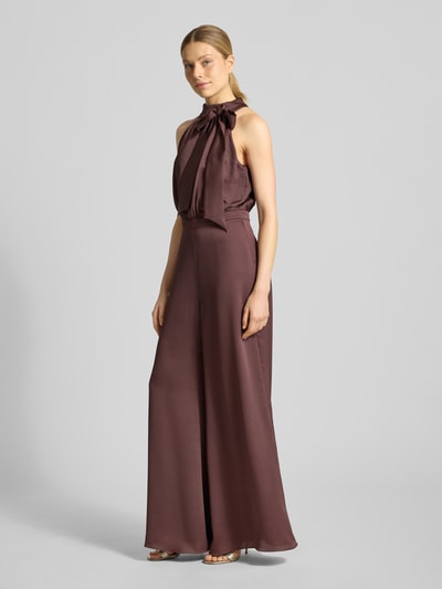 Modelka nosi Jumpsuit mit Zierschleife od Swing, brązowy, strukturalny wzór, krój slim fit, bez rękawów, elastyczny materiał, całościowy widok z przodu, szerokość w rozmiarze 36: 37 cm, długość tyłu: 43 cm, długość całkowita: 150 cm, długość nogawki: 82 cm.
