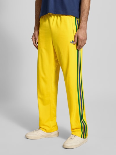 Mannelijk model draagt Straight fit Sweatpants met logo-stitching model 'Firebird' van adidas Originals in geel met steekzakken, elastische band, binnenbeenlengte bij maat M: 40 cm, zijkantstrepen, ganzekörperaanzicht van voren.