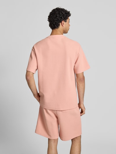 Männermodel trägt Oversized Fit T-Shirt mit Strukturmuster von KARL KANI, Baumwoll-Mix, hellrosafarbene Textur, Ganzkörperansicht Rückansicht.