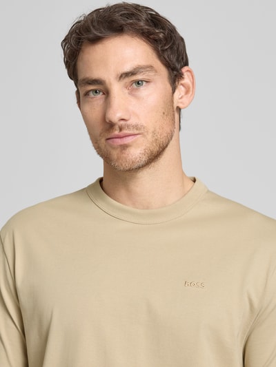 Mężczyzna model nosi Regular Fit T-Shirt aus reiner Baumwolle Modell 'H-TAUT 15' von BOSS, gładki beżowy kolor, okrągły dekolt, krótki rękaw, materiał bawełna, zbliżenie na górną część ciała.
