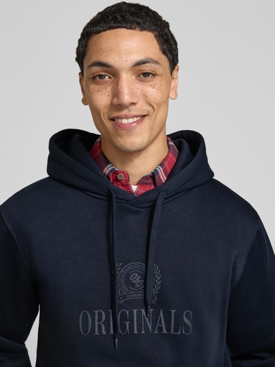 Männermodel trägt Hoodie aus Baumwoll-Mix Modell 'FREDERIKS' von JACK & JONES, dunkelblau, Label-Print, Nahaufnahme Oberkörper.