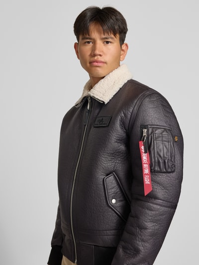 Männermodel trägt Bomberjacke mit Label-Patch und Kentkragen von Alpha Industries, schwarze Struktur, Teddyfellkragen, Nahaufnahme Oberkörper. Herren Bomberjacke, Regular Fit, Reißverschluss, Ärmeltasche mit Label-Detail, Eingrifftaschen mit Druckknopf, gerippte Abschlüsse.