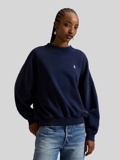 Vrouwenmodel draagt 'Oversized Sweatshirt aus Baumwoll-Mix' van Polo Ralph Lauren, effen donkerblauw, logostiksel, ribboorden, lange mouwen, katoenmix sweatstof, voorkant bovenlichaam close-up.