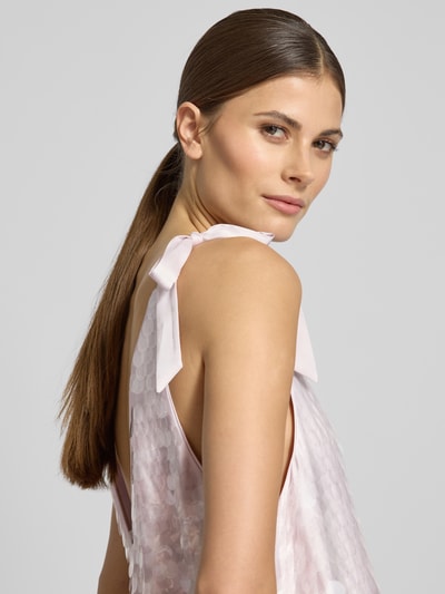 Frauenmodel trägt Relaxed Fit Kleid mit Allover-Paillettenbesatz von Jake*s Cocktail in Hellrosa mit Zierschleifen, Nahaufnahme Oberkörper.