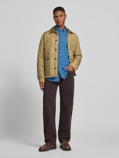 Männermodel trägt Slim Fit Jeanshemd aus reiner Baumwolle von Barbour in Denim-Optik, durchgehende Knopfleiste, Label-Stitching-Applikation, Langarm, Button-Down-Kragen, 1-Knopf-Manschette, leicht abgerundeter Rumpfabschluss, Farbe mittelblau, Ganzkörperansicht von vorne.