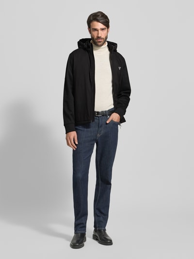 Männermodel trägt schwarzen Windbreaker mit Zweiwege-Reißverschluss von Guess, Regular Fit, Kapuze, Label-Detail, Reißverschlusstaschen, Ganzkörperansicht von vorne.