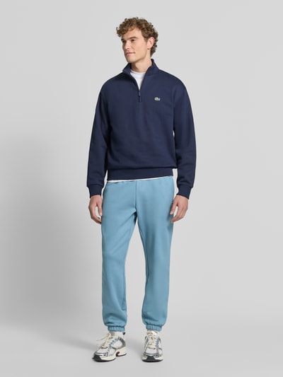 Männermodel trägt Regular Fit Sweathose aus Baumwoll-Mix von Lacoste in Hellblau, kombiniert mit dunklem Oberteil, Ganzkörperansicht von vorne. Herren Sweathose von Lacoste.