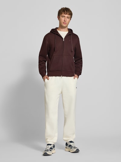 Männermodel trägt Sweatjacke mit Label-Stitching und Känguru-Tasche von Champion im Regular Fit, braun, Baumwoll-Mix, Ganzkörperansicht von vorne.