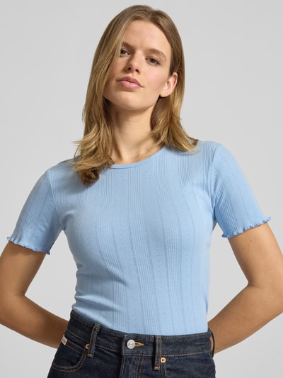 Modelka nosi Slim Fit T-Shirt aus Baumwoll-Mix Modell 'TENNA' od Only, jednokolorowa, krój slim fit, okrągły dekolt, krótkie rękawy z falbanką, bawełniany materiał, widok na górną część ciała z przodu.