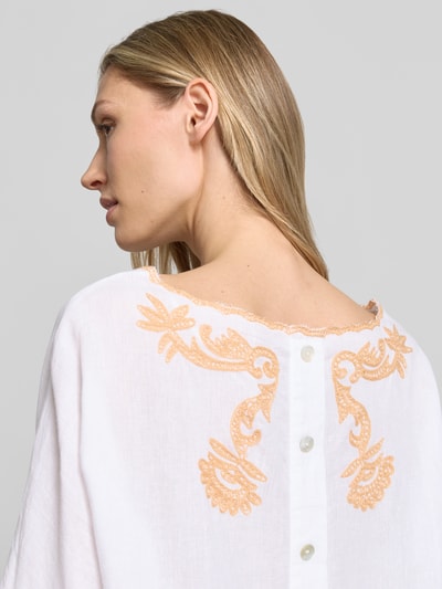 Frauenmodel trägt Blusenshirt mit Leinen-Anteil und Motiv-Stitching von Christian Berg Woman, weiß mit apricotfarbenem Muster, Viskose-Mix, Loose-Fit, U-Boot-Ausschnitt mit Kontrastkante, Rückenlänge 55 cm, Ärmellänge 34 cm, Detailaufnahme Rückansicht.