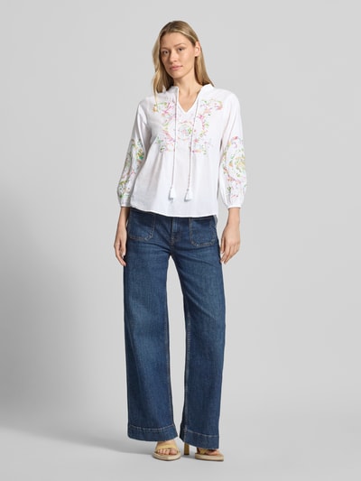 Frauenmodel trägt Bluse mit Schlüsselloch-Ausschnitt und Schnürung von Emily Van den Bergh aus Reine Baumwolle, Straight Fit, weiße Farbe mit floralem Muster, 3/4-Arm und abgerundetem Saum, Ganzkörperansicht von vorne. Rückenlänge bei Größe 36: 62 cm, Ärmellänge: 50 cm.