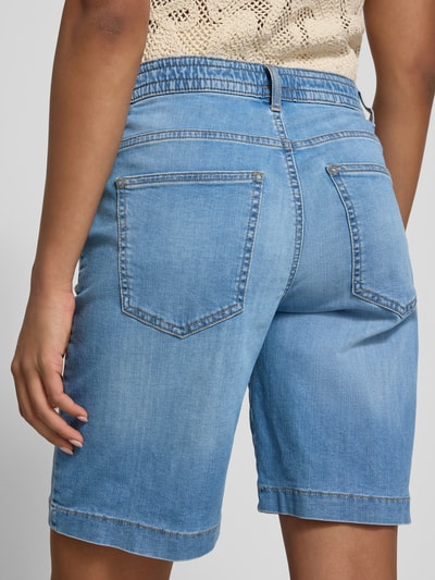 Frauenmodel trägt Regular Fit Jeansshorts aus Baumwoll-Mix Modell 'MAINE B' von Brax in heller Denim-Optik mit Label-Patch, 5-Pocket-Design, Ganzkörperansicht Rückansicht.