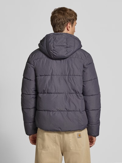 Männermodel trägt Steppjacke mit Kapuze und Reißverschluss von Superdry in Dunkelgrau, wattierte Struktur, Ganzkörperansicht Rückansicht, Regular Fit, verdeckter Reißverschluss, Knopfleiste, Stehkragen, Rückenlänge 71 cm, Schulterbreite 50 cm, Brustweite 56 cm, Ärmellänge 83 cm.