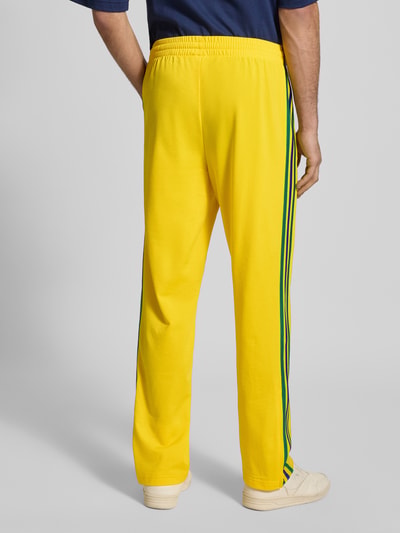 Männermodel trägt gele Sweatpants met Logostitching, straight fit, steekzakken met ritssluiting, elastische band, model 'Firebird' van adidas Originals, binnenbeenlengte maat M 40 cm, ganzkörperansicht rückansicht