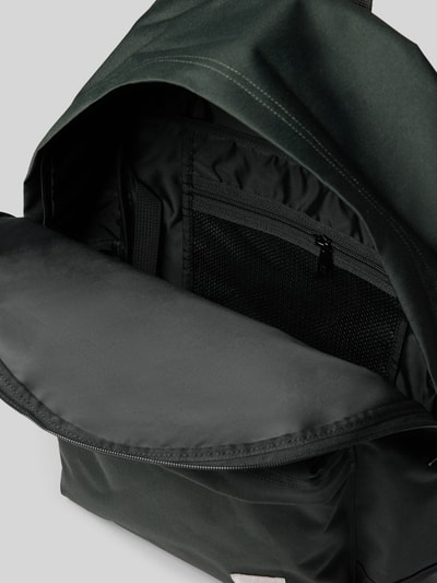 Produktfoto, Rucksack mit Label-Patch Modell 'Jake' von Carhartt Work In Progress, schwarzes Material, Mesh-Innenfach, glatte Textur, Hauptfach mit Zweiwege-Reißverschluss, Außenfach sichtbar, neutraler Hintergrund, für Männer