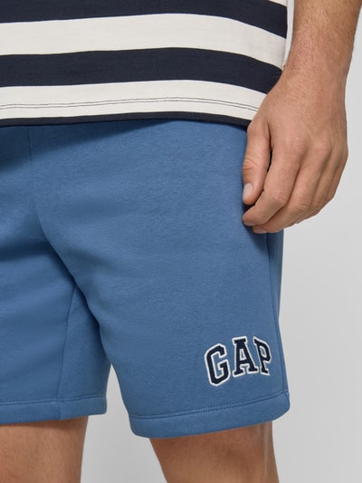 Männermodel trägt Sweatshorts mit Logo und elastischem Bund von GAP in Blau aus Baumwoll-Mix mit Eingrifftaschen, Nahaufnahme Oberschenkel.