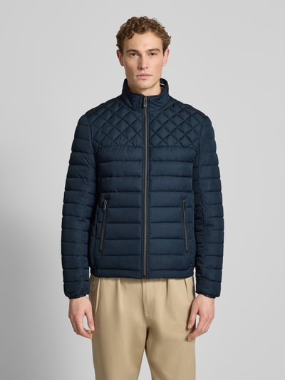 Mężczyzna nosi Slim Fit Steppjacke mit gefüttertem Kragen von Christian Berg Men, kolor granatowy, kieszenie zapinane na zamek błyskawiczny, krój slim fit, podszewka na kołnierzu, elastyczne zakończenia rękawów, długość tyłu w rozmiarze M: 68 cm, szerokość ramion w rozmiarze M: 47 cm, szerokość w rozmiarze M: 52 cm, długość rękawów w rozmiarze M: 68 cm, widok całej sylwetki z przodu
