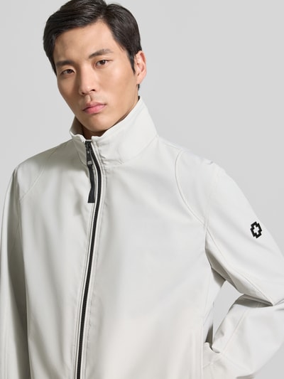 Męski model nosi Regular Fit Funktionsjacke aus wasserdichtem Material Modell 'LUCCA' von Strellson, gładkie jasnoszare tkaniny, logo z metalu, stojący kołnierz, zamek błyskawiczny, długie rękawy z regulacją, krój regular fit, ochrona przed wodą i wiatrem, detaliczne ujęcie górnej części ciała z przodu.