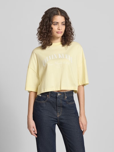 Frauenmodel trägt Cropped T-Shirt mit Logo-Print von Calvin Klein Jeans in Hellgelb, reine Baumwolle, Rundhalsausschnitt, Ganzkörperansicht von vorne.