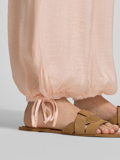Frauenmodel trägt Relaxed Fit Stoffhose aus Viskose-Mix von Gina Tricot, semitransparent, Tunnelzug, Nahaufnahme Beinbereich.