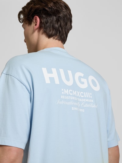 Männermodel trägt Loose Fit T-Shirt aus reiner Baumwolle Modell 'NALONO_F' von Hugo Blue in Hellblau mit Logo-Details, Ganzkörperansicht Rückansicht.