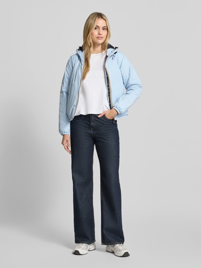 Frauenmodel trägt kurtka Regular Fit z nadrukiem z logo Model 'CLAUDETTE' od K-WAY, kolor jasnoniebieski, kaptur z tunelem, elastyczne wykończenia, długość tyłu w rozmiarze S: 59 cm, szerokość ramion w rozmiarze S: 39 cm, szerokość w rozmiarze S: 51 cm, długość rękawów w rozmiarze S: 63 cm, gładka powierzchnia, prosty fason, widoczne szwy, Ganzkörperansicht von vorne.