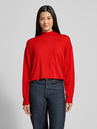 Vrouwenmodel draagt rode oversized schippertrui met opstaande kraag van pure scheerwol, geribde boorden, Drykorn MATHISA, frontaal totaalbeeld.