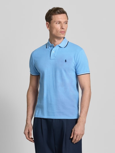 Männermodel trägt Slim Fit Poloshirt aus reiner Baumwolle von Polo Ralph Lauren in Hellblau mit Logo-Stitching und Kontraststreifen, Ganzkörperansicht von vorne.