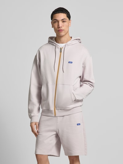 Männermodel trägt Relaxed Fit Sweatjacke aus reiner Baumwolle Modell 'Nadarasi' von HUGO in Optik: Unifarben mit Reißverschluss, Label-Print, Kapuze mit Tunnelzug, langarm, Ärmelabschluss und Rumpfabschluss gerippt, Materialverarbeitung: Sweat, Ganzkörperansicht von vorne.