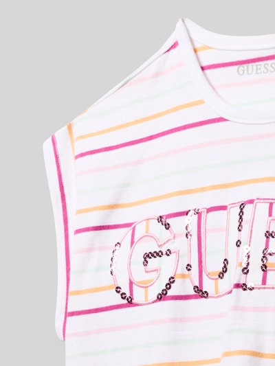 Mädchen trägt Kinder T-Shirt mit bunten Streifen, Logo-Stitching und Paillettenbesatz von Guess, Baumwoll-Mix mit Stretch-Anteil, Nahaufnahme Oberkörper.