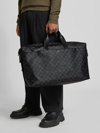 Männermodel trägt Weekender mit verstellbarem Schulterriemen von JOOP! Collection in Schwarz mit Label-Detail, Ganzkörperansicht von vorne.