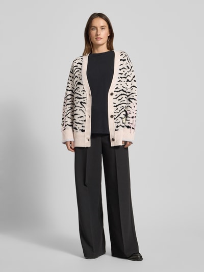 Frauenmodel trägt Strickjacke mit Knopfleiste von Marc Cain, Reine Baumwolle, Lockerer-Schnitt, Gerippte-Abschlüsse, V-Ausschnitt, Farbkontrastmuster in Beige und Schwarz, locker fallender Stoff, Kombi mit schwarzer Hose, Ganzkörperansicht von vorne.