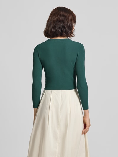Frauenmodel trägt grüne Slim Fit Strickjacke aus Viskose-Mix Modell 'WKDTENNIS' von Weekend Max Mara, cremefarbener Rock, Ganzkörperansicht Rückansicht, Damen Strickjacke von Max Mara.