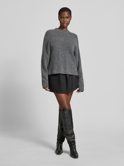 Frauenmodel trägt Pullover in Strick-Optik aus Alpaka-Mix von black palms mit Relaxed-Fit, Rundhalsausschnitt und elastischen Ärmelabschlüssen, Rückenlänge bei Größe S 62 cm, dunkle Farben, weiche Textur, Ganzkörperansicht von vorne.