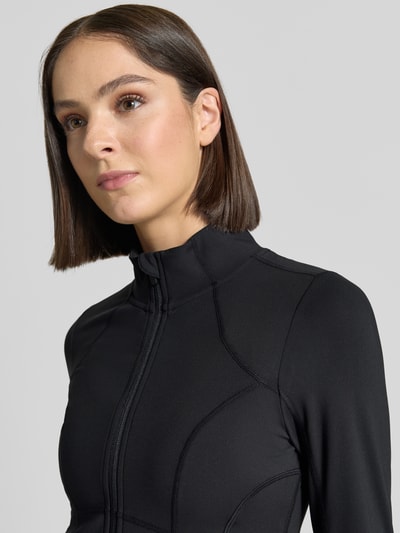 Vrouwenmodel draagt Slim Fit jack met opstaande kraag Model 'STORM' van Fabletics, zwart, ritssluiting, gladde textuur, Nahaufnahme Oberkörper. Dames jack, Ruglengte maat S: 45 cm, schouderbreedte: 35 cm, borstwijdte: 42 cm, mouwlengte: 68 cm.