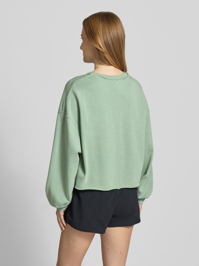 Frauenmodel trägt Relaxed Fit Pullover mit Logo-Stitching Modell 'Chill' von Nike aus grünem Baumwoll-Mix, elastische Ärmelabschlüsse, Rundhalsausschnitt, Ganzkörperansicht Rückansicht.