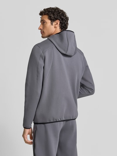 Męski model nosi szarą kurtkę treningową Regular Fit Trainingsjacke mit Baumwoll-Anteil Modell 'Unstoppable' od Under Armour, gładka tekstura, widok całej sylwetki z tyłu, kurtka treningowa męska