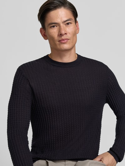 Männermodel trägt Strickpullover mit Struktur-Muster von Emporio Armani, dunkle Farbe, Material-Mix mit Woll-Anteil, Nahaufnahme Oberkörper.
