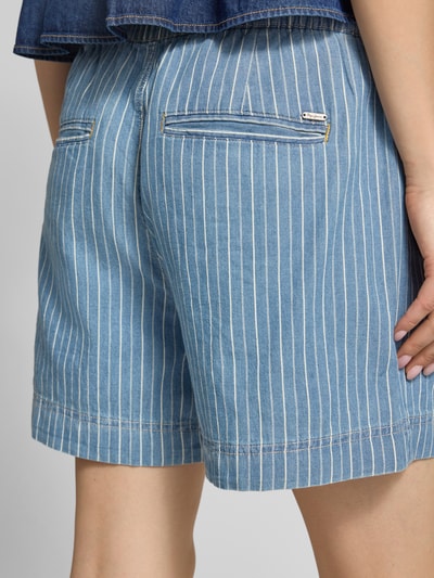 Frauenmodel trägt Jeansshorts aus reiner Baumwolle Modell 'MW' von Pepe Jeans, blau mit weißen Streifen, Ganzkörperansicht Rückansicht.