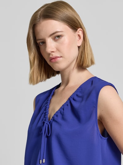 Kobieta modelka nosi Regular Fit Bluse mit Zierschleife von Marc Cain, dekolt w serek, tunel, krój bez rękawów, długość tyłu 62 cm w rozmiarze 36, zbliżenie na górną część sylwetki