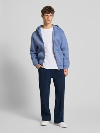 Męski model nosi Sweathose mit Biese und Varsiety Embleme od REVIEW, granatowa bawełna z domieszką stretchu, luźny krój, widok całej sylwetki z przodu.