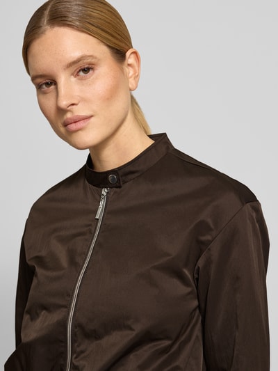 Männermodel trägt Cropped Jacke mit Zweiwege-Reißverschluss von monari in Dunkelbraun, Stehkragen, Knopfverschluss, Szerokość w rozmiarze 36: 50 cm, długość tyłu: 49 cm, szerokość klatki piersiowej: 44 cm, długość rękawa: 56 cm, gładka tekstura, Nahaufnahme Oberkörper.