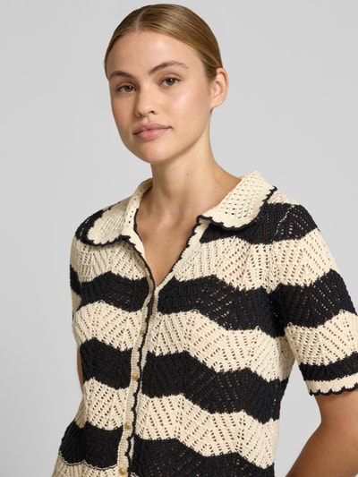 Modelka nosi Regular Fit Cardigan aus reiner Baumwolle Modell 'GOLDEN COVE' von Vero Moda, krój regular fit, dzianina bawełniana, wzór w paski, czarno-kremowe kolory, dekolt w serek, krótki rękaw, dzianinowa tekstura, wygląd swetrowy, widok z przodu, zbliżenie na górną część ciała.